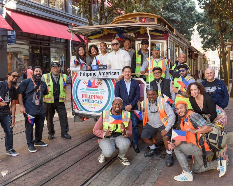 People standing and kneeling on and in front of a stationary cable car and on the tracks.
