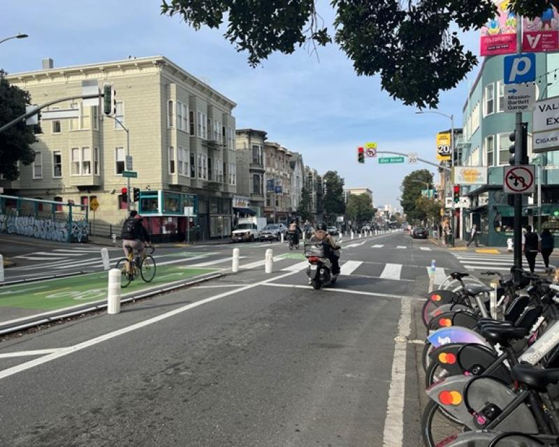 People bike through a center-running protected bikeway in the middle of a street with motorcycles and cars in the outer lanes.